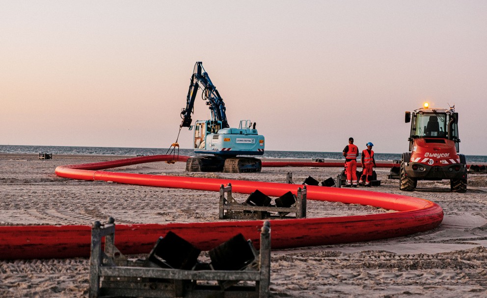 Baustelle auf Norderney mit roten Rohren, zwei Arbeitern, einem roten und einem hellblauen Bagger
