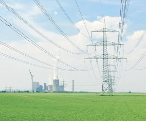 Das Bild zeigt eine Stromtrasse und Windräder in einem grünen Feld - im Hintergrund ein Kraftwerk