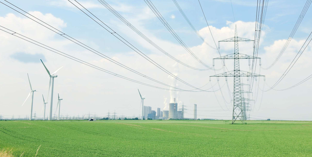 Das Bild zeigt eine Stromtrasse und Windräder in einem grünen Feld - im Hintergrund ein Kraftwerk