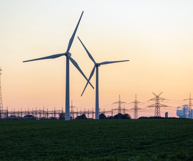 Windräder vor einer Umspannanlage, einem Kraftwerk und Strommasten im Hintergrund