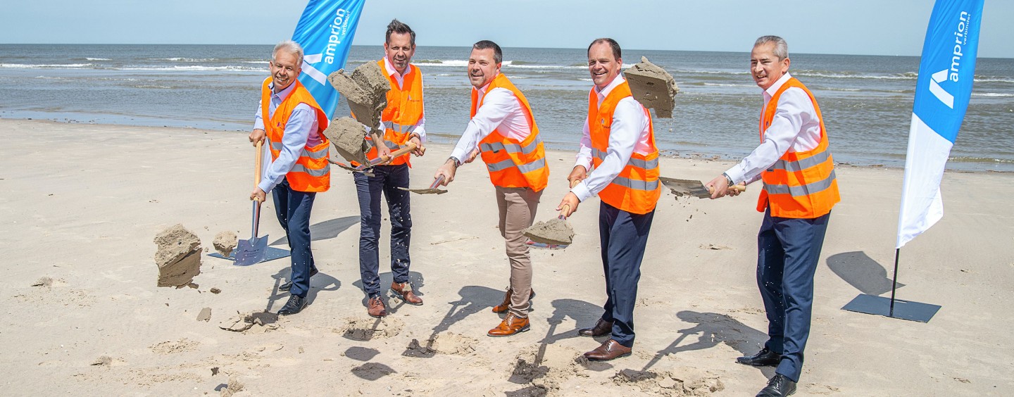 Das Bild zeigt eine Gruppe von fünf Männern, die auf einem Strand dabei sind, Sand mit Schaufeln aufzuwerfen.