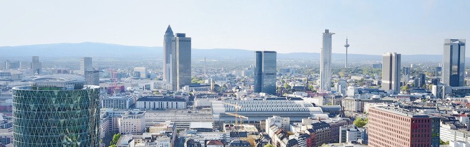 Panorama von Frankfurt am Main mit modernen Hochhäusern, darunter der Messeturm und der Europaturm. Im Vordergrund ist das auffällige, grün verglaste Westhafen Tower-Gebäude mit seiner rautenförmigen Glasstruktur zu sehen.