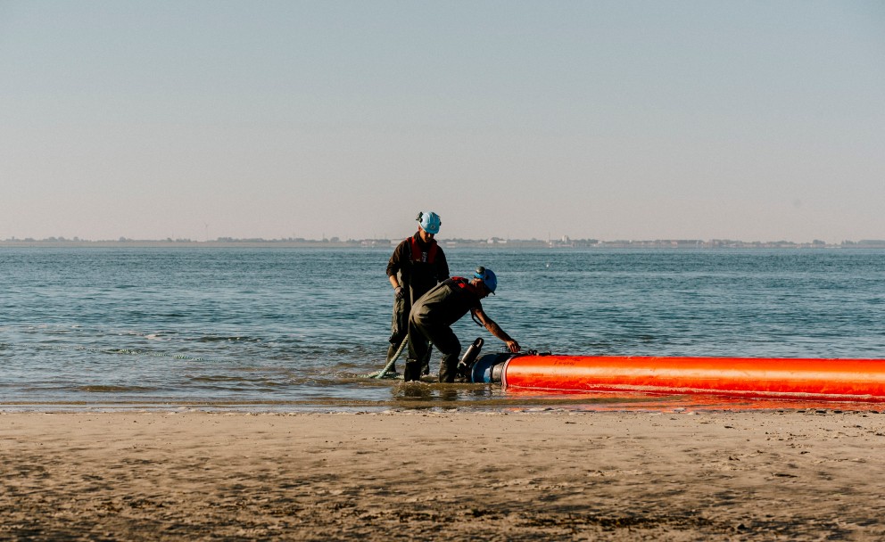Zwei Monteure am Strand, sie bringen die Muffen an die Rohrleitungen an.