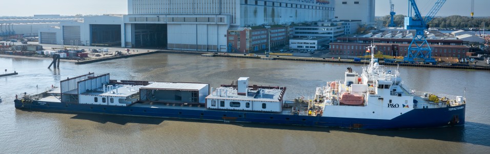 Beladenes Frachtschiff vor Meyer Werft im Wasser vor dem Werftgebäude.