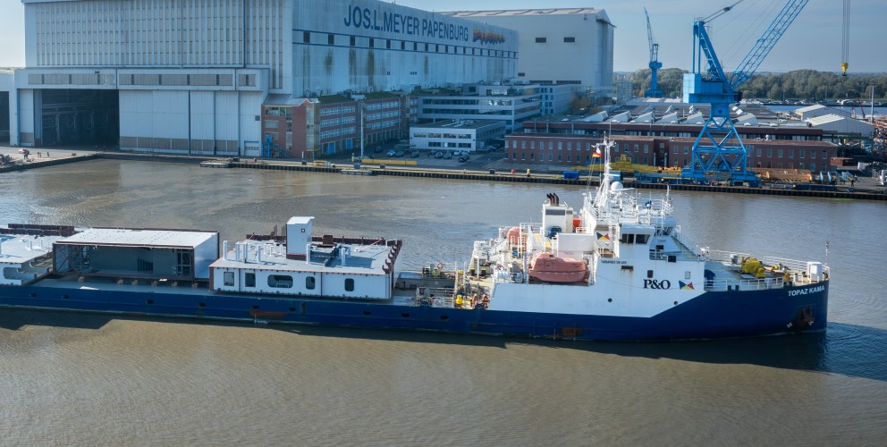 Beladenes Frachtschiff vor Meyer Werft im Wasser vor dem Werftgebäude.