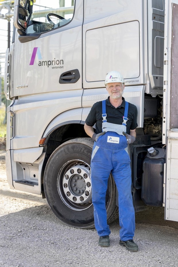 Ein Mann in Arbeitskleidung und Schutzhelm steht vor einem LKW mit Amprion-Logo.